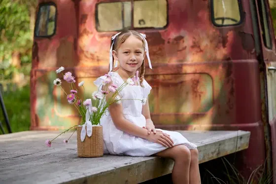 Little girl in a white lace dress with a jar of flowers on the flatbed truck at Premier Studio