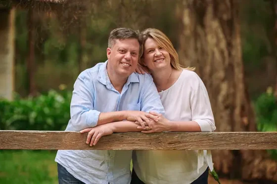Couple in a light blue shirt and cream top leaning on the timber fence at Premier Studio