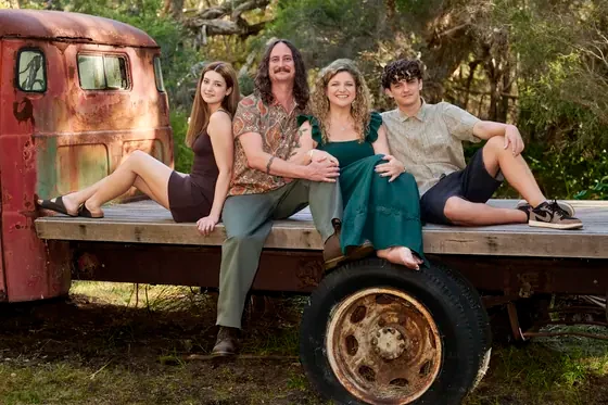 Family of four in dark teal, olive and black seated on the flatbed truck at Premier Studio