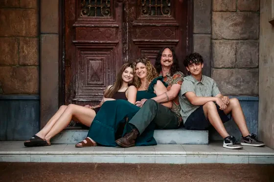 Family of four with mum in an emerald dress seated before the red timber doors at Premier Studio