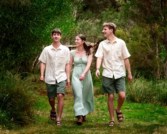 Mum in a sage dress with two sons in cream shirts and olive shorts walking through the bush at Premier Studio