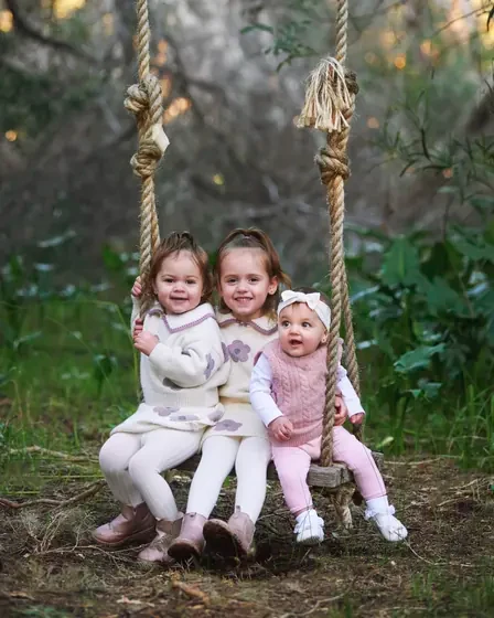 Two little girls in pink and cream knits sharing the rope swing at Premier Studio