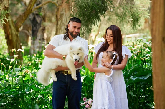 Family of three in white with dad in navy denim holding their Samoyed among the lilies at Premier Studio