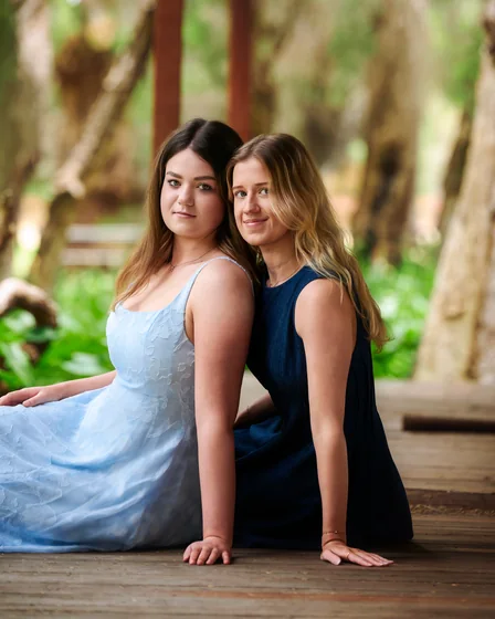 Two sisters in light blue and navy dresses seated on the timber deck at Premier Studio