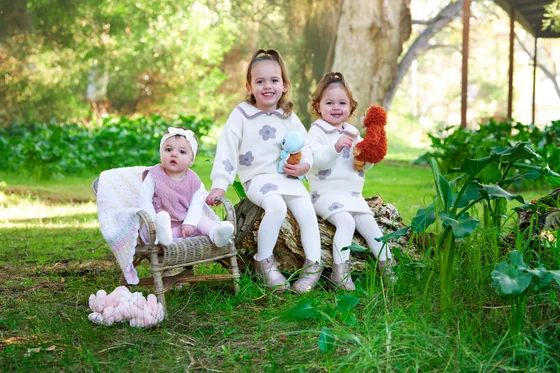 Two little girls in cream and blush knits seated among the arum lilies at Premier Studio