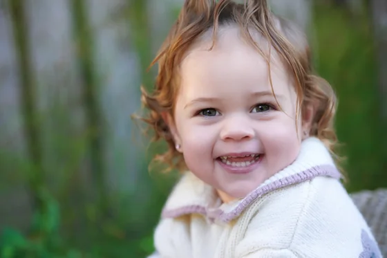 Baby girl in a cream and pink knit laughing, close portrait at Premier Studio