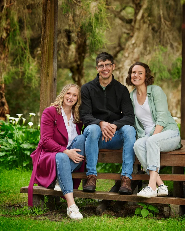 A large family photographed outdoors wearing blues, greens and tan