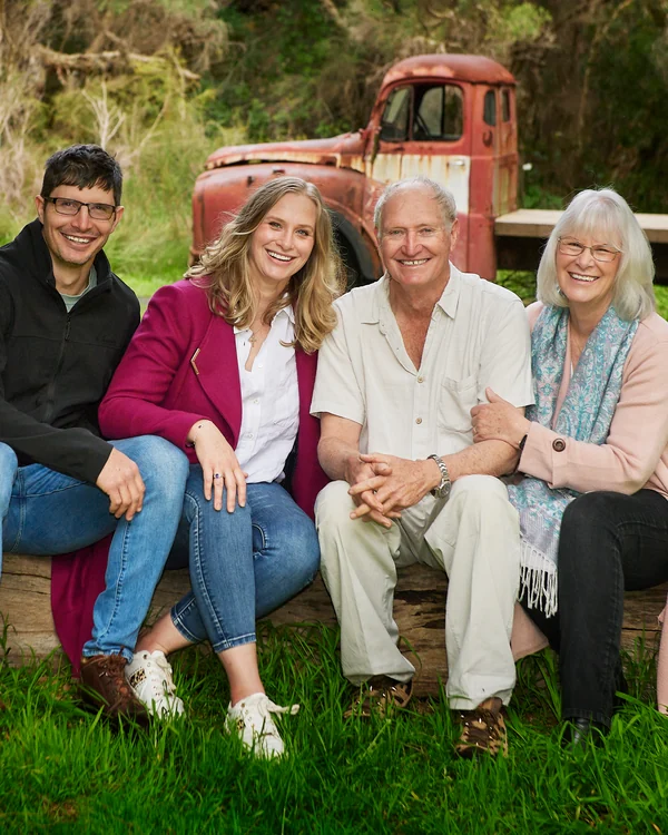 A large family photographed outdoors wearing blues, greens and tan