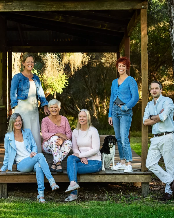 A large family photographed outdoors wearing blues, greens and tan