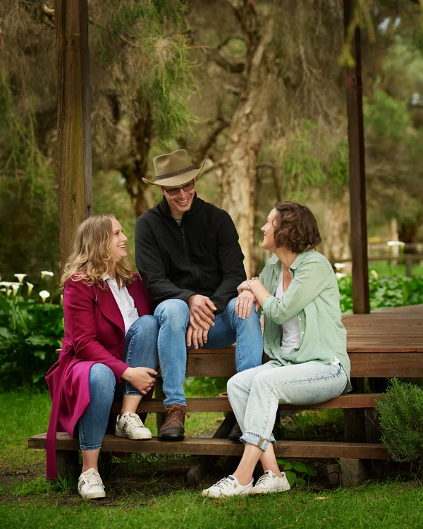 A large family photographed outdoors wearing blues, greens and tan